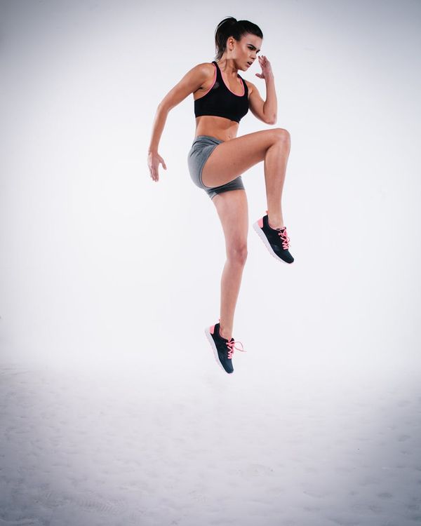 Woman in activewear performing a dynamic cardio movement in a modern studio.